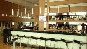 A modern bar area with a long counter, multiple stools, and a variety of bottles and glasses on shelves. - DoubleTree by Hilton Ankara Ankamall (Ankara)