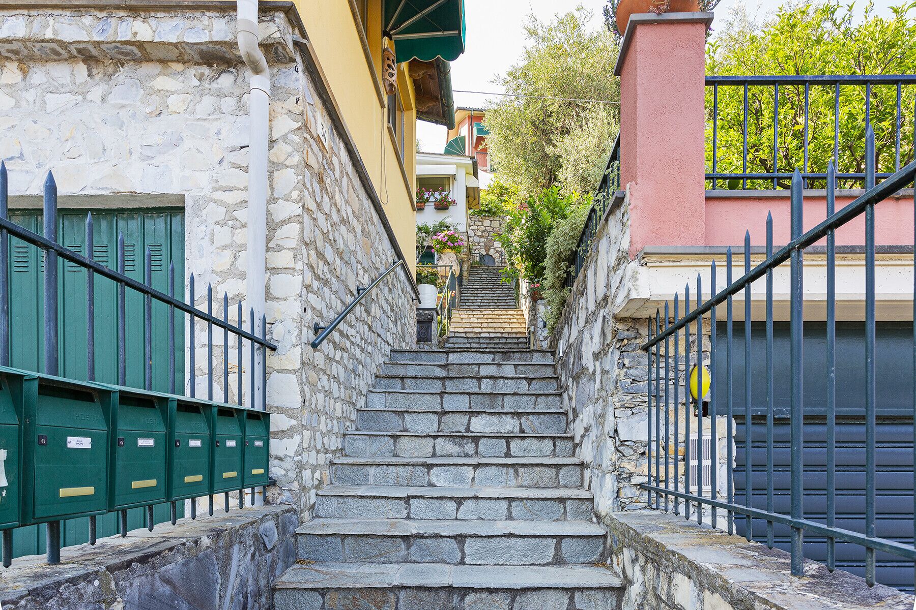 A stone staircase leading to a building with a green fence on one side and a black gate on the other.