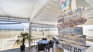 A beachside restaurant with wooden tables and chairs, a potted plant, and a view of the beach. - Miramare Residence (Navodari)