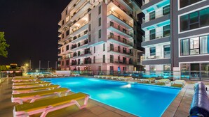 A swimming pool with lounge chairs, surrounded by multi-story buildings with balconies and illuminated windows. - Miramare Residence (Navodari)