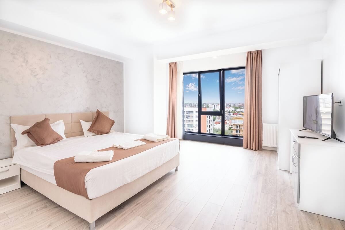 Una habitación de hotel moderna con una cama grande, televisión y ventana con vista a la ciudad.