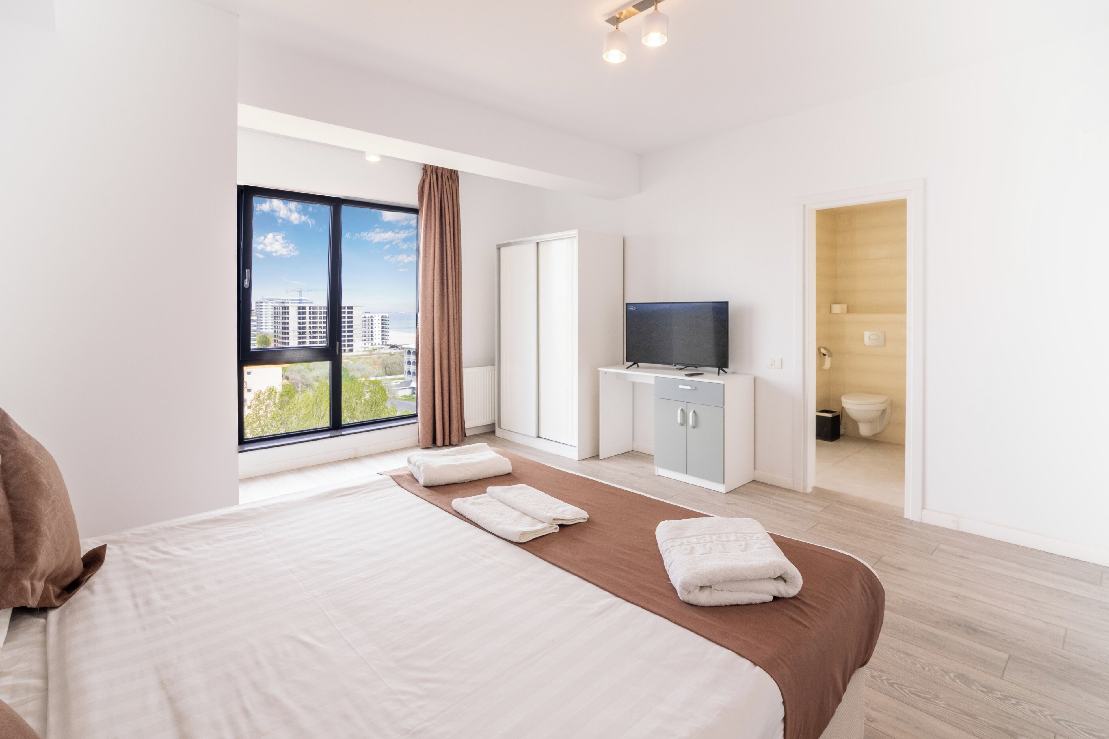 A modern hotel room with a large bed, a television, a bathroom, and a view of the city.