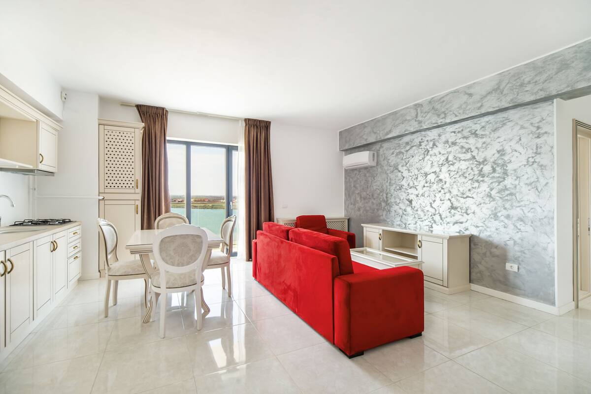 Una cocina moderna con armarios blancos, una mesa de comedor con sillas, un sofá rojo y un ventanal con cortinas.