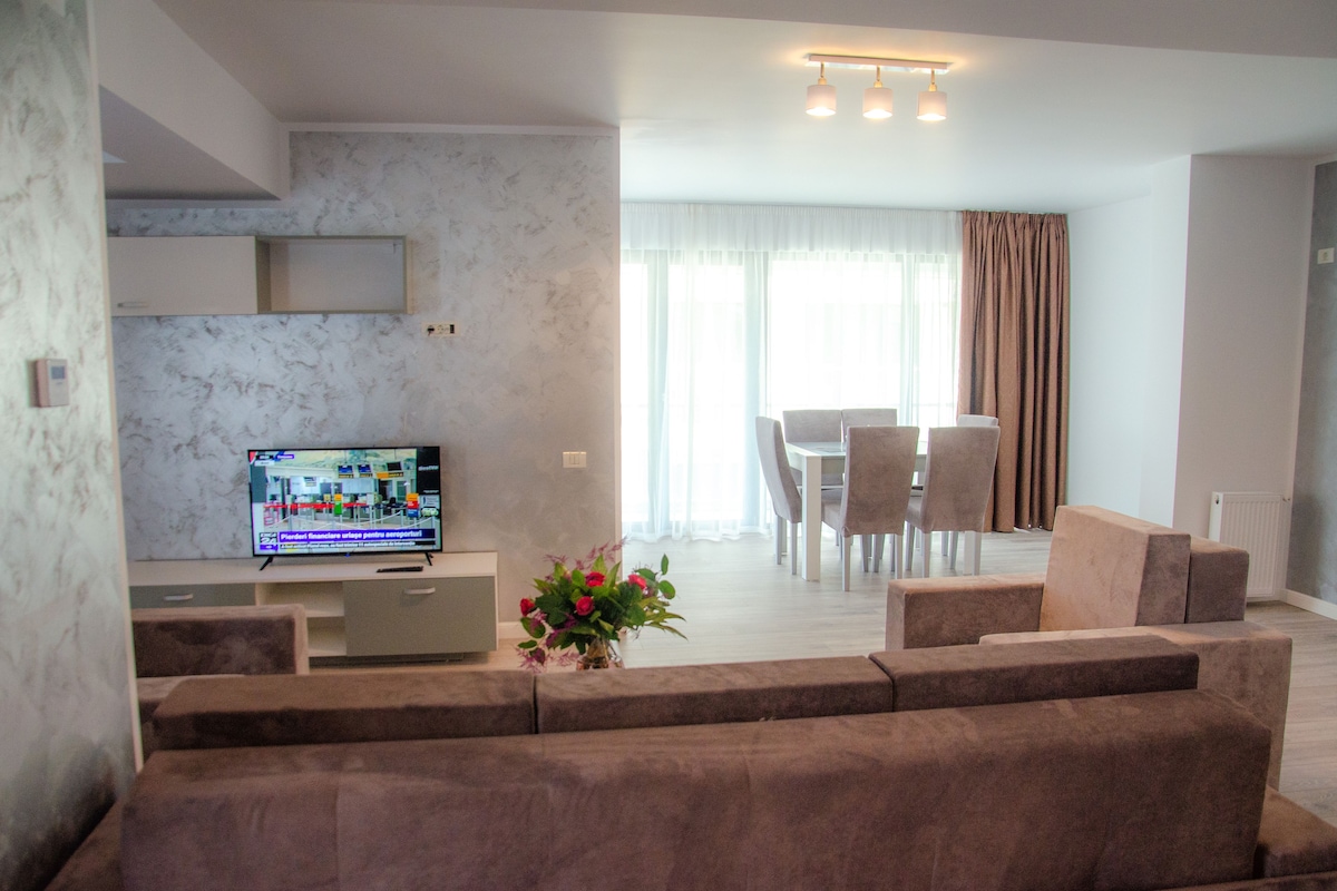 A modern living room with a sofa, a TV, and a dining area with chairs and a table.