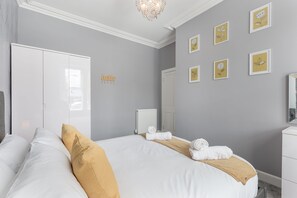 A hotel room with two beds, a white wardrobe, a radiator, and framed artwork on the wall.