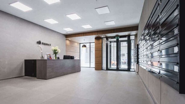 A modern reception area with a reception desk, a wall-mounted storage unit, and a large glass door leading outside.