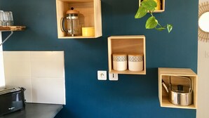 A kitchen with wooden shelves holding a coffee maker, a yellow container, and a plant. There is a toaster on the counter. - The lagoon terrace (Saint Leu)