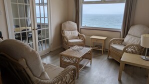 Een woonkamer met rieten meubilair, uitzicht op zee en een deur naar een balkon.