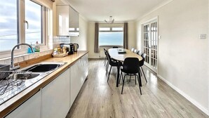 Een moderne keuken met uitzicht op zee, een eethoek met stoelen, en een groot raam.