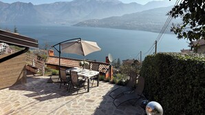 Een terras met een tafel, stoelen, een barbecue en uitzicht op een meer en bergen.