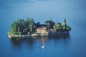 An island with a large building surrounded by trees and a small boat in the water. - Modern house: privacy, air conditioning and unobstructed view of Lake Iseo ★★★★★ (Italia)