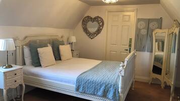Un dormitorio con cama con dosel, una mesita de noche con lámpara, cómoda, espejo y puerta decorada con un adorno en forma de corazón.
