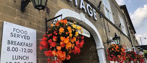 A building with a sign reading "THE STAGE" and a menu board listing breakfast, lunch, and dinner times.