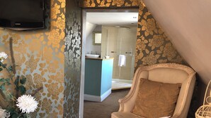 A hotel room with a large mirror, a bathroom with a glass shower, a decorative chair, and a vase with flowers. - The Deeping Stage (Peterborough)