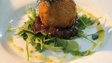 A plated dish with a spherical item topped with greens and a sauce.