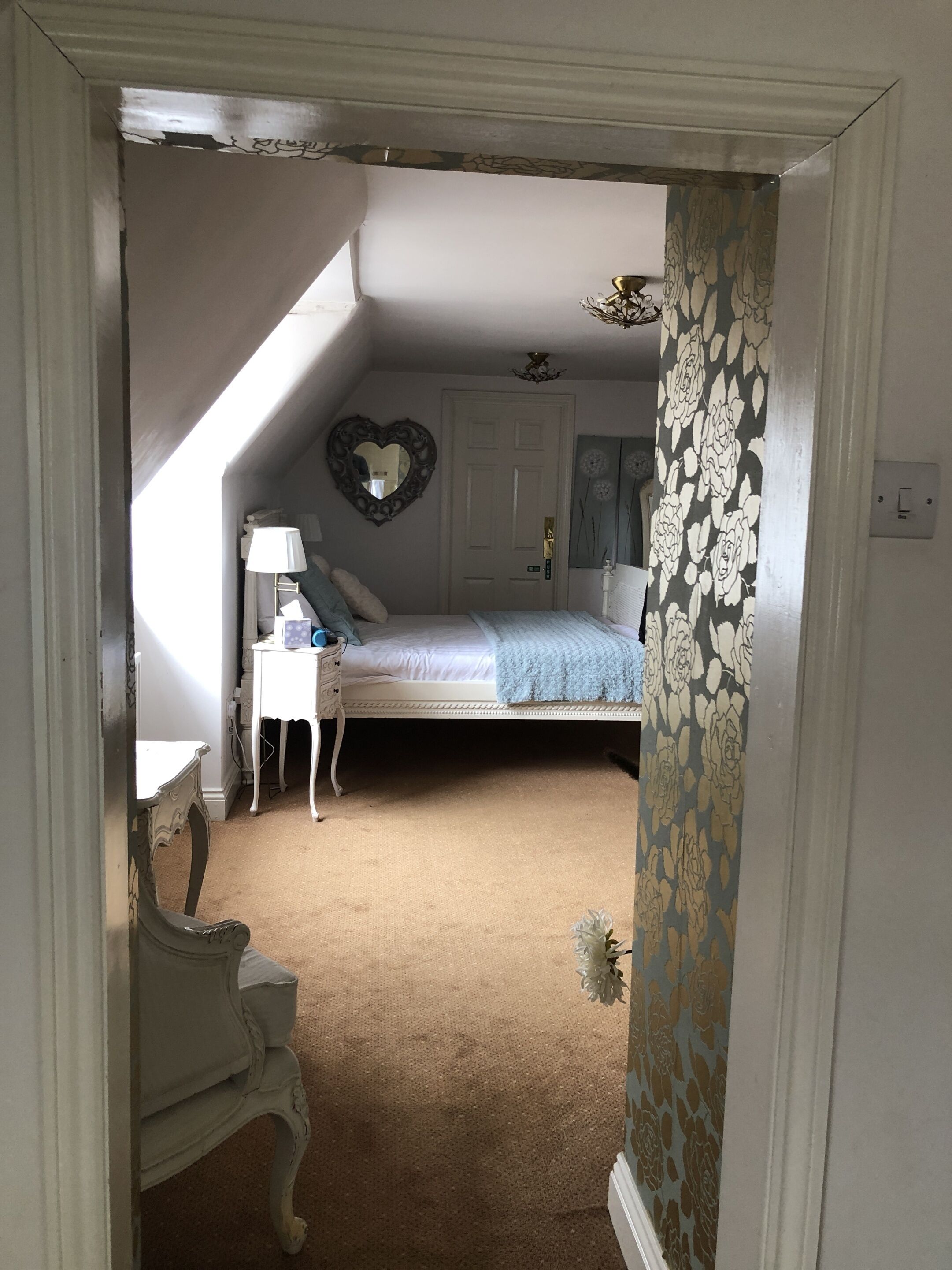 A bedroom with a white bed, a dresser, a nightstand, and a heart-shaped mirror on the wall.