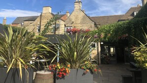 A courtyard with stone buildings, potted plants, and a sign reading "The Stage". - The Deeping Stage (Peterborough)