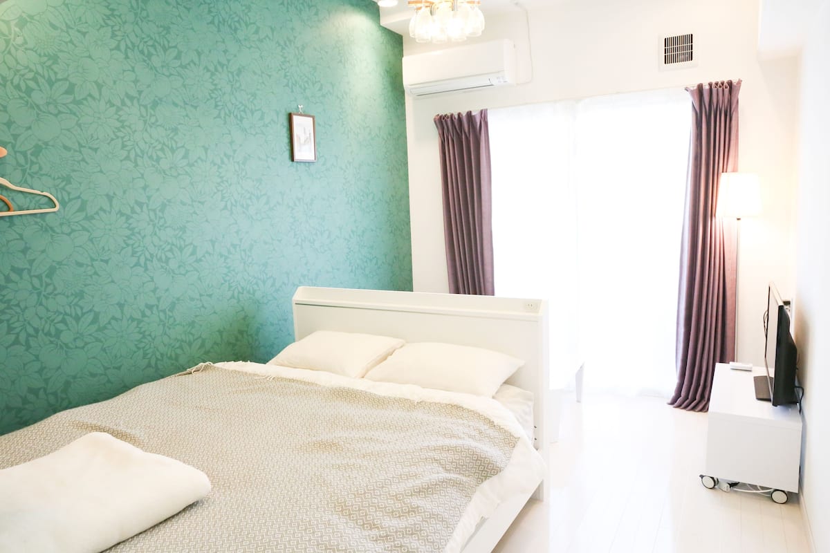 A neatly made bed with a patterned bedspread, a bedside table with a lamp, and a wall-mounted air conditioner.