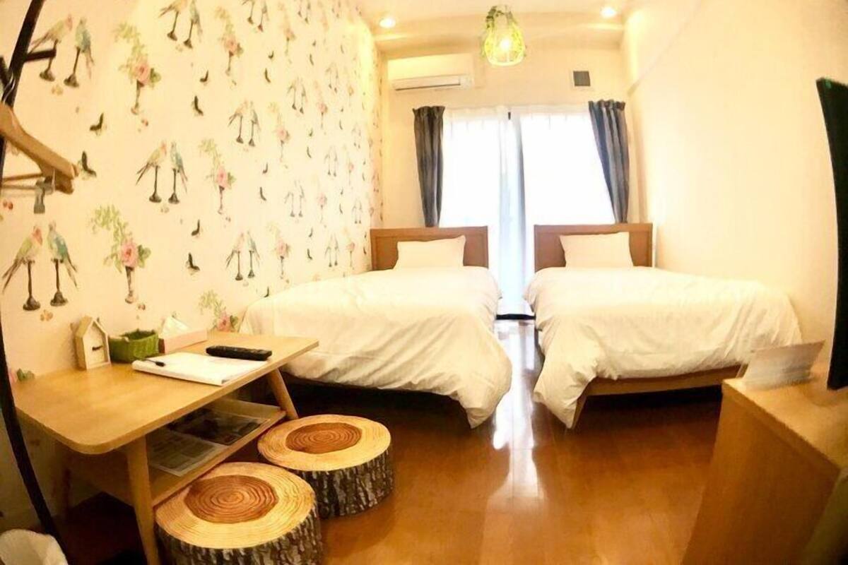 A hotel room with two beds, a wooden desk, and a window with curtains.