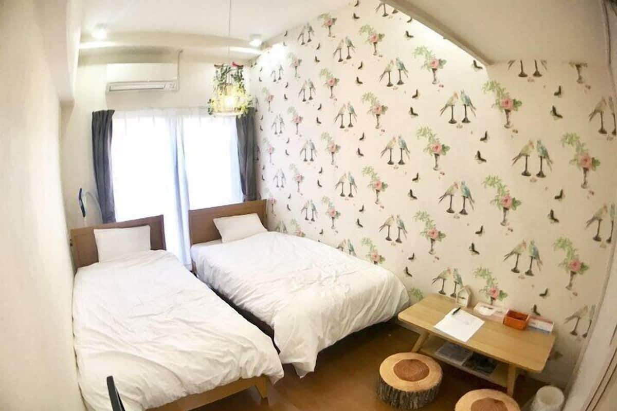 A room with two beds, a small table, and a hanging plant.