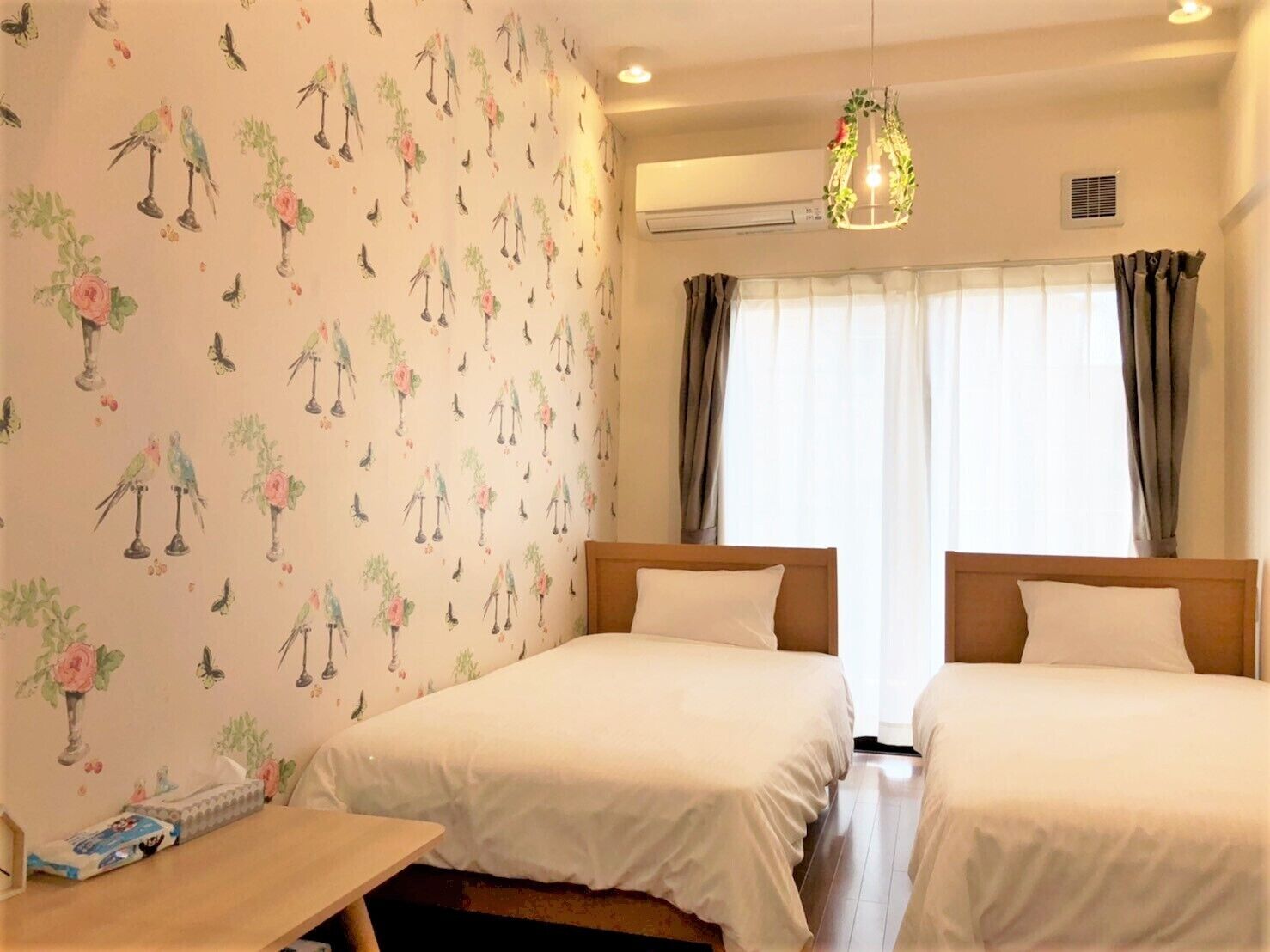 A hotel room with two beds, a wooden table, and a window with curtains.