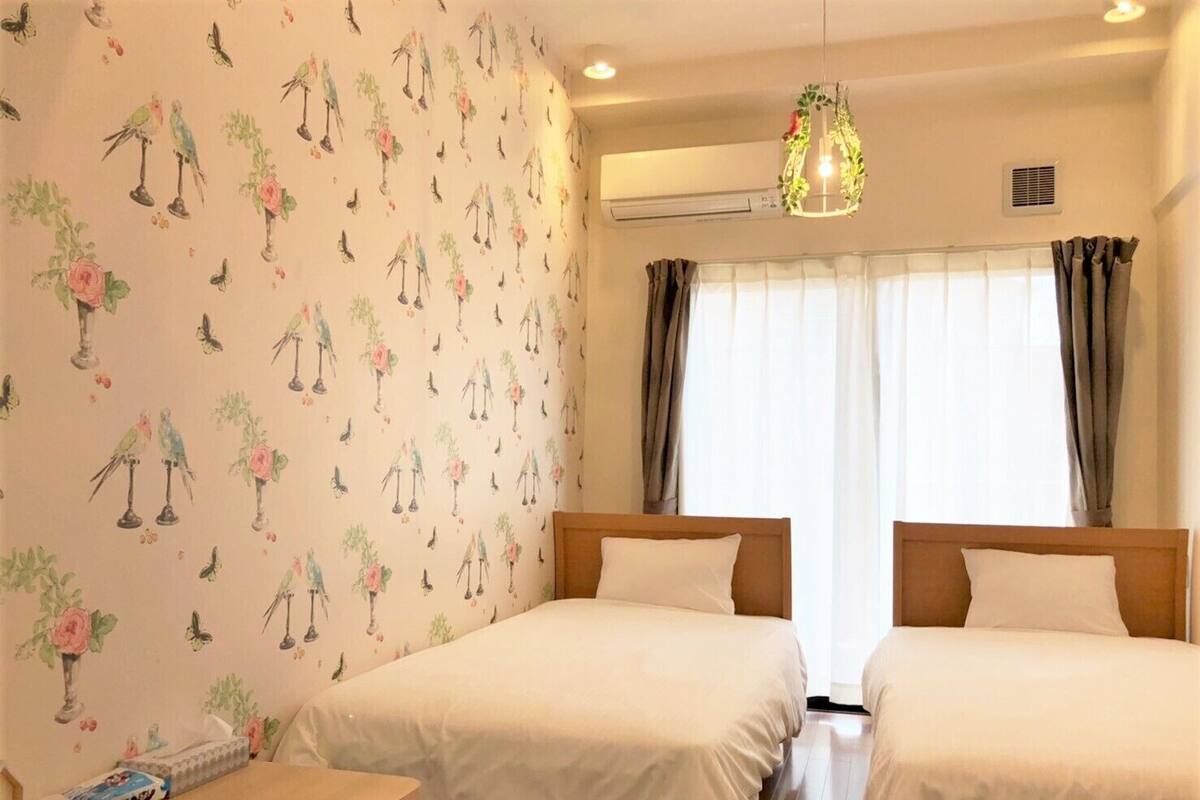 A hotel room with two beds, a wooden table, and a window with curtains.