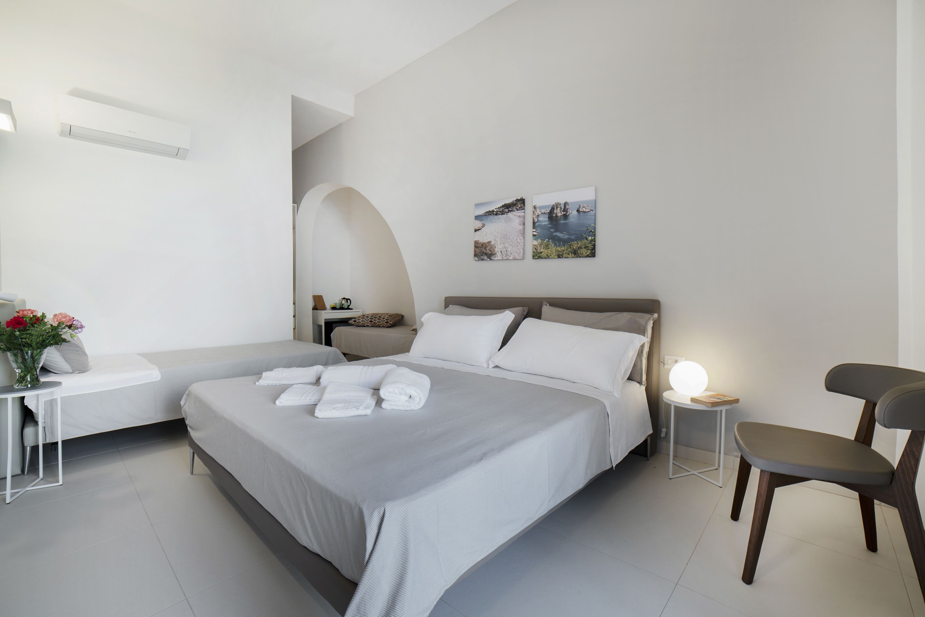 Una habitación de hotel moderna con una cama grande, una mesita de noche con lámpara, una silla y dos obras de arte colgadas en la pared.