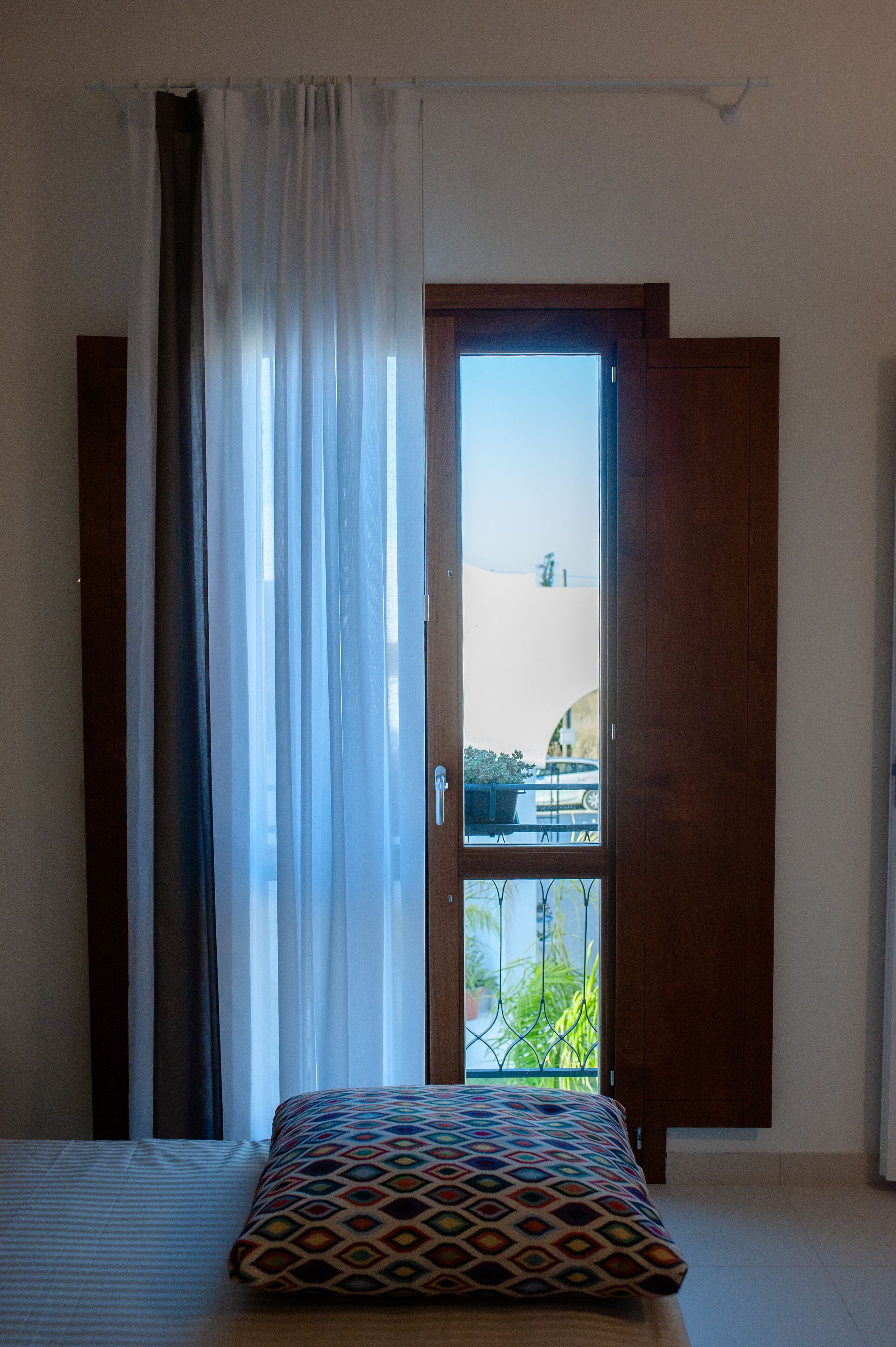 A bedroom with a bed, a window with curtains, and a view of the outside.