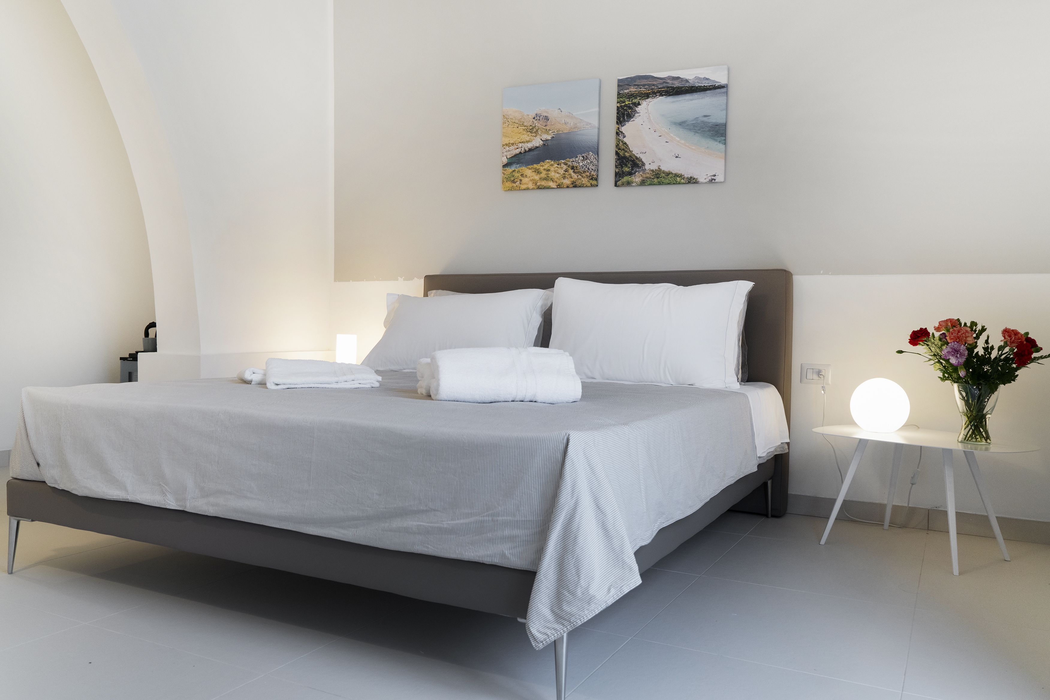 A modern bedroom with a bed, bedside tables, and a nightstand with a lamp.