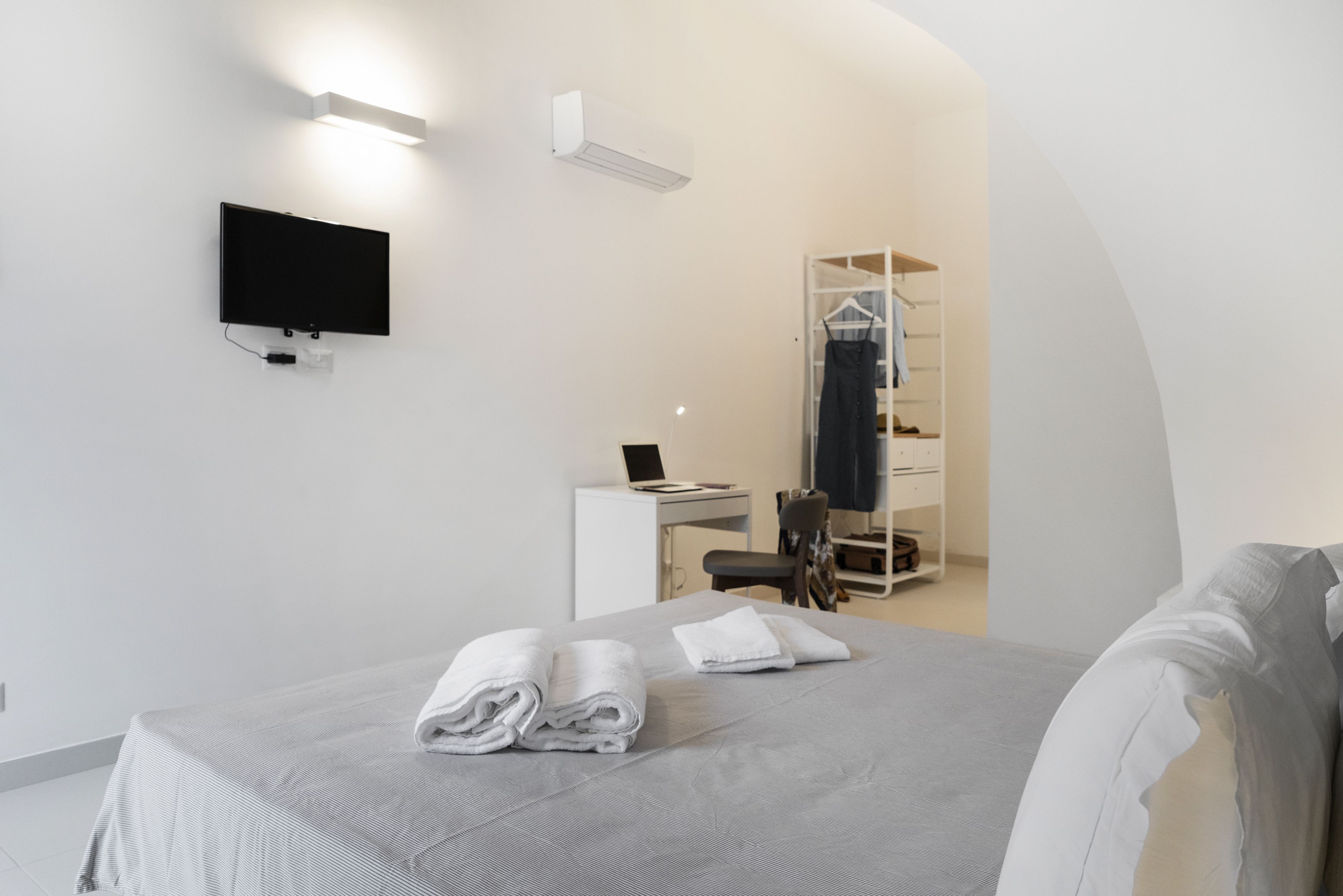 Ein modernes Hotelzimmer mit einem Bett, einem Schreibtisch, einem Sessel, einem Fernseher und einem begehbaren Kleiderschrank.