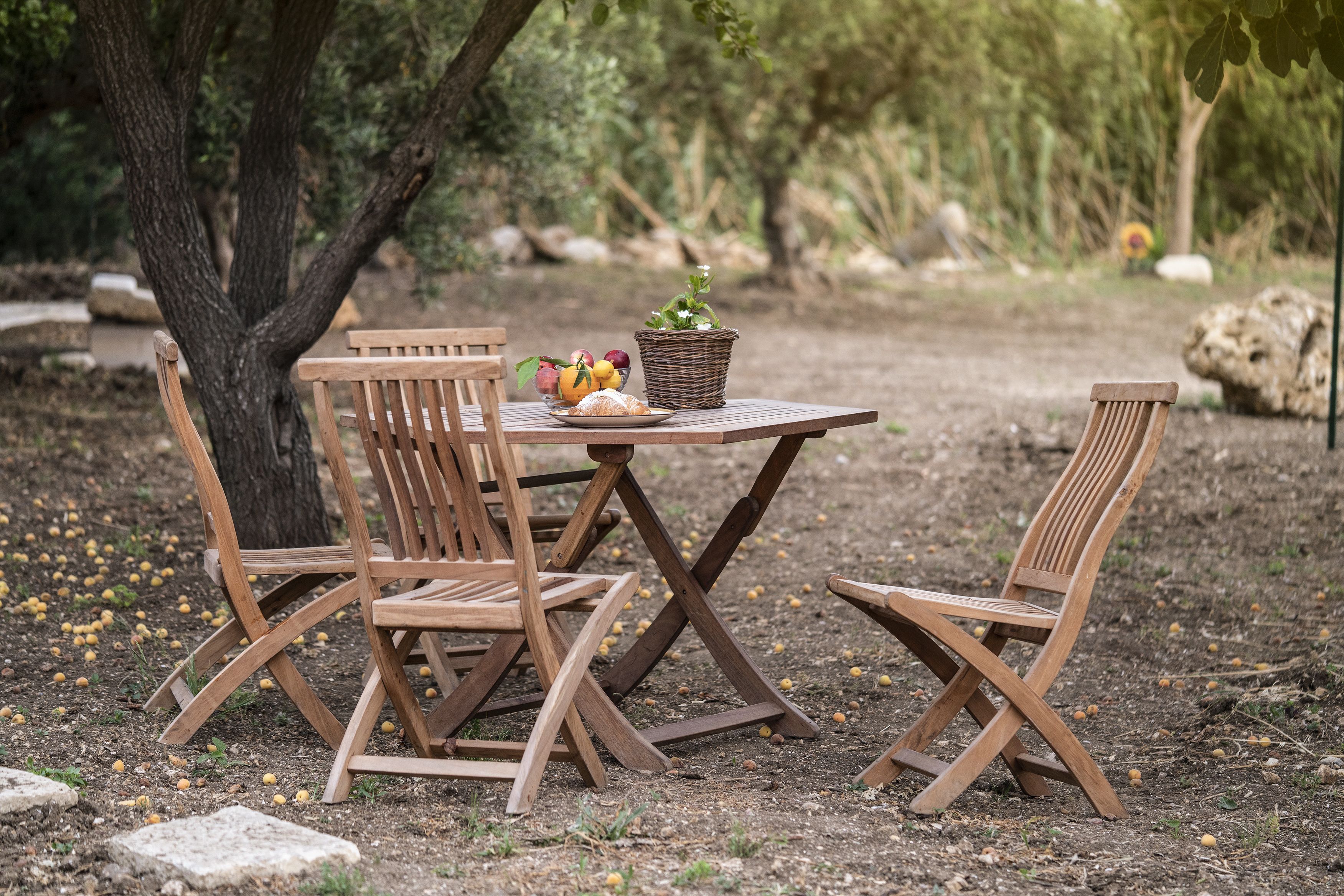 A wooden table with chairs, a basket of fruit, and a potted plant in an outdoor setting.
