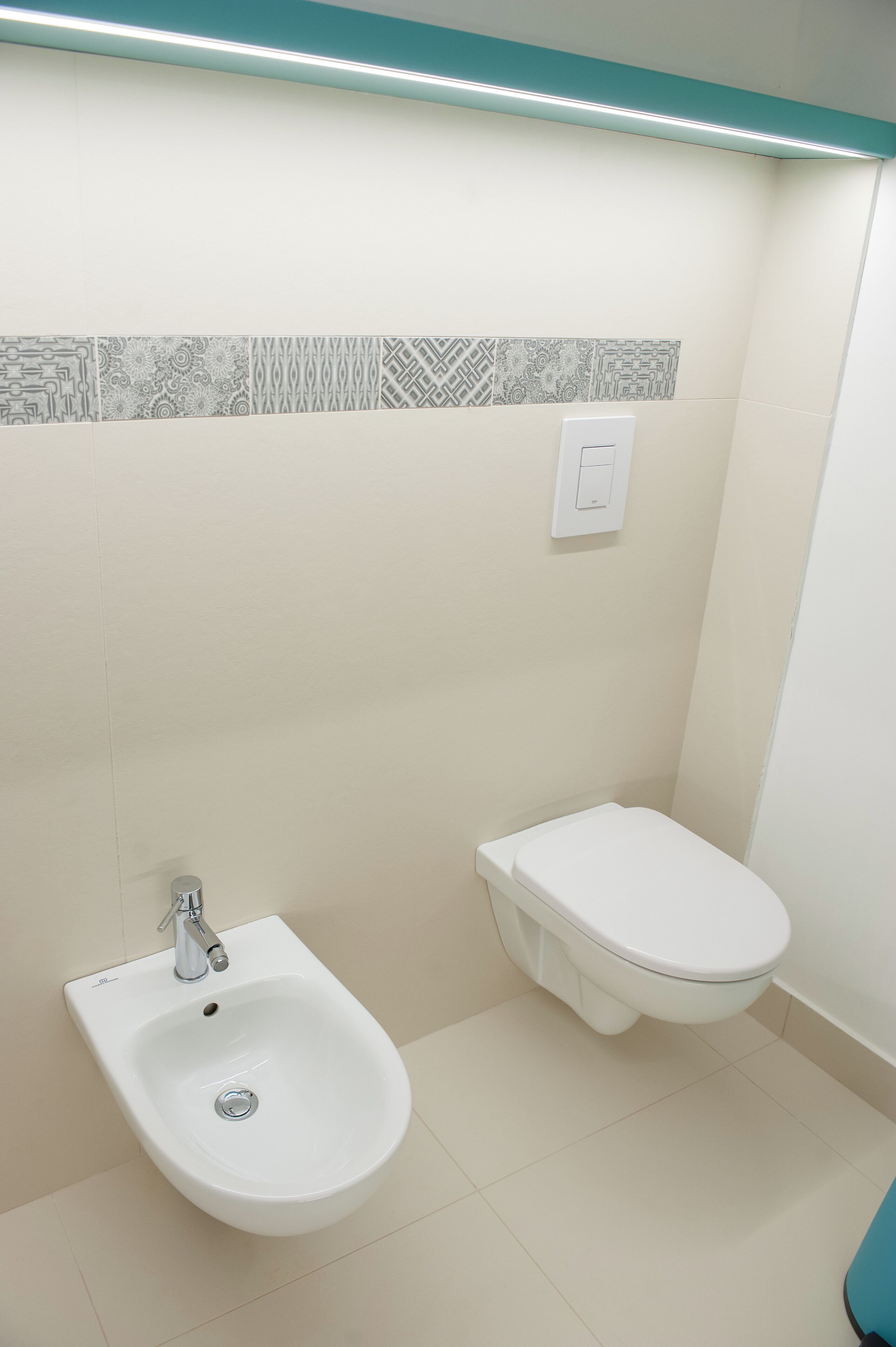 A bathroom with a bidet, a toilet, and a wall-mounted light fixture.