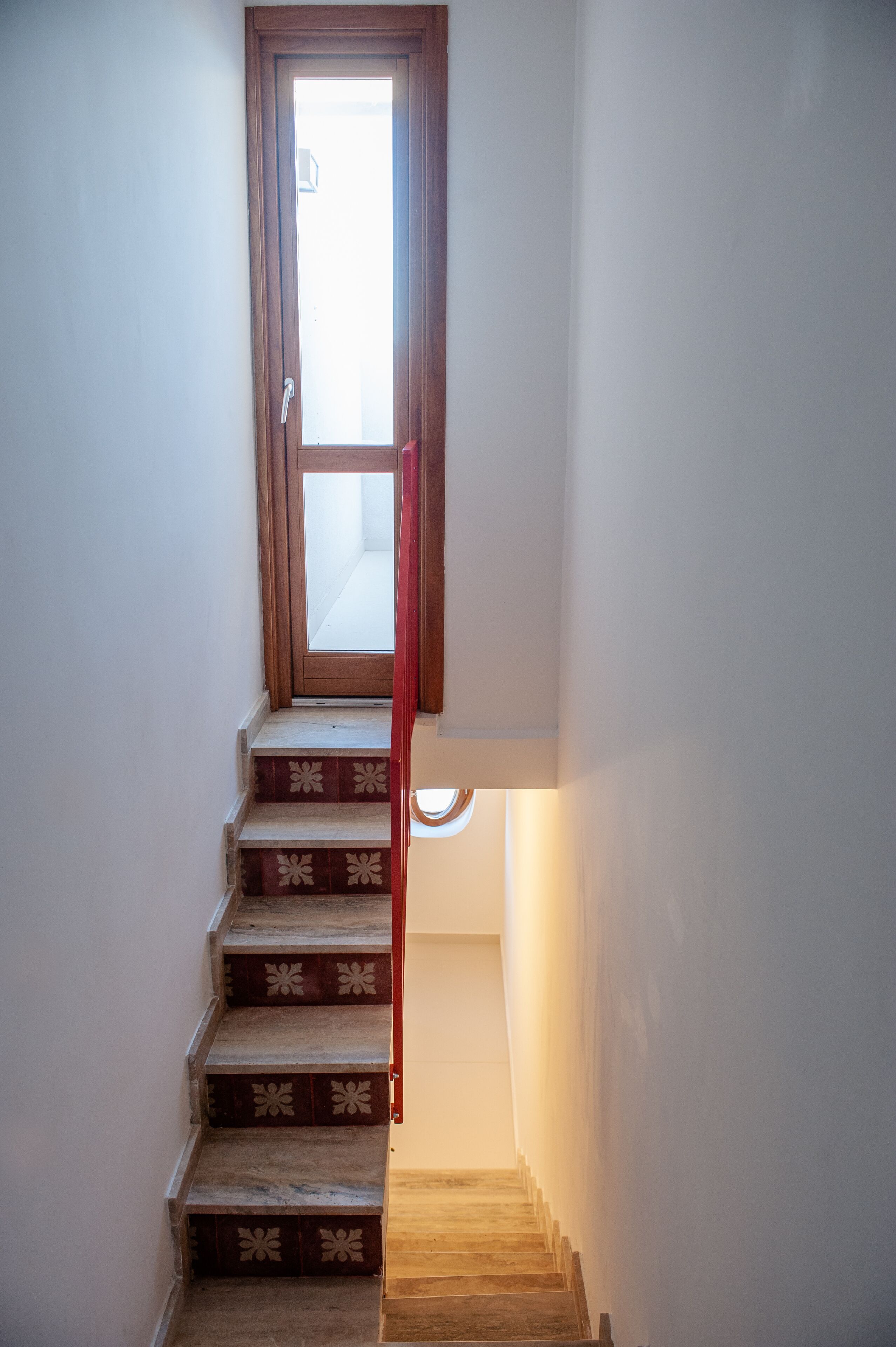 Un escalier étroit aux marches décorées mène à une porte surmontée d’une fenêtre.