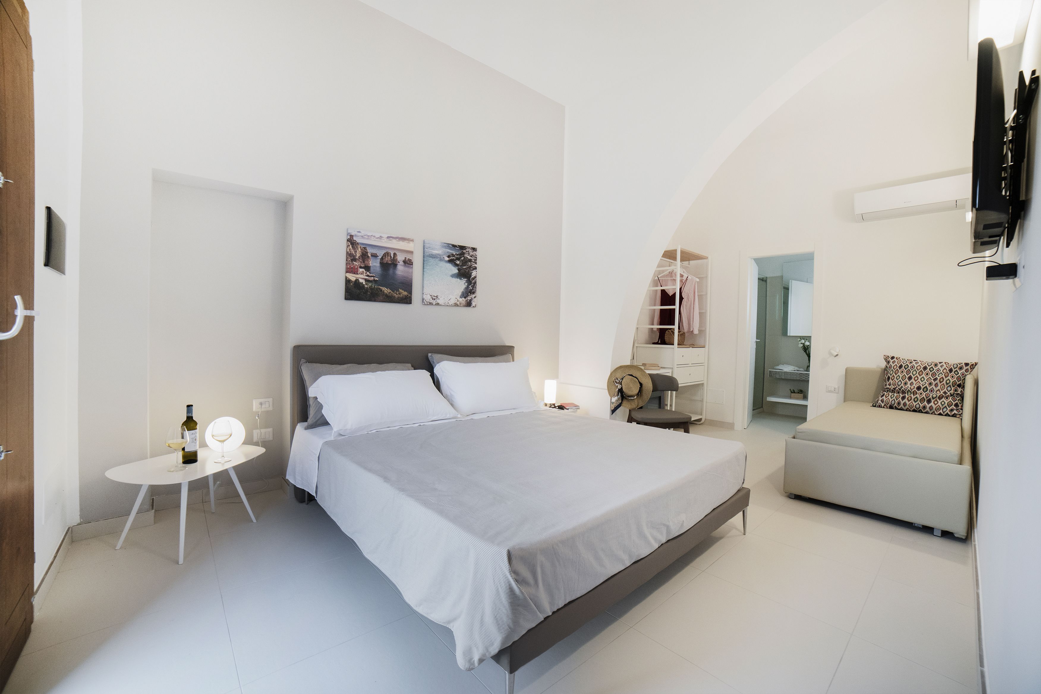 A modern bedroom with a large bed, a small table with a bottle and glass, and a sofa.