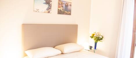 A hotel room with a large bed, two wall-mounted pictures, a vase with flowers, and a window with curtains.