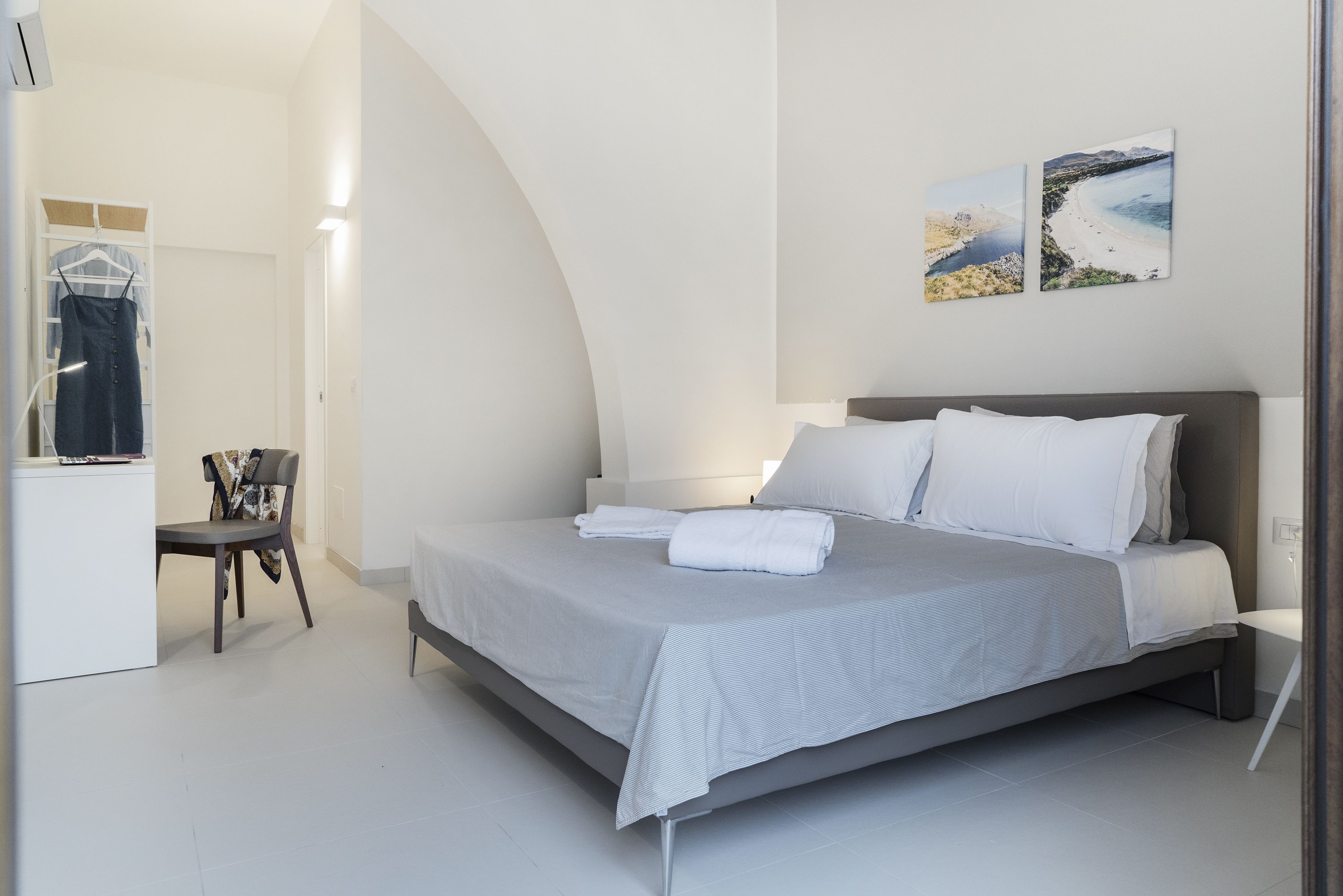 Un dormitorio moderno con una cama, una silla, un escritorio y dos cuadros colgados en la pared.