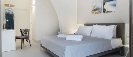 Un dormitorio moderno con una cama, una silla, un escritorio y dos cuadros colgados en la pared.