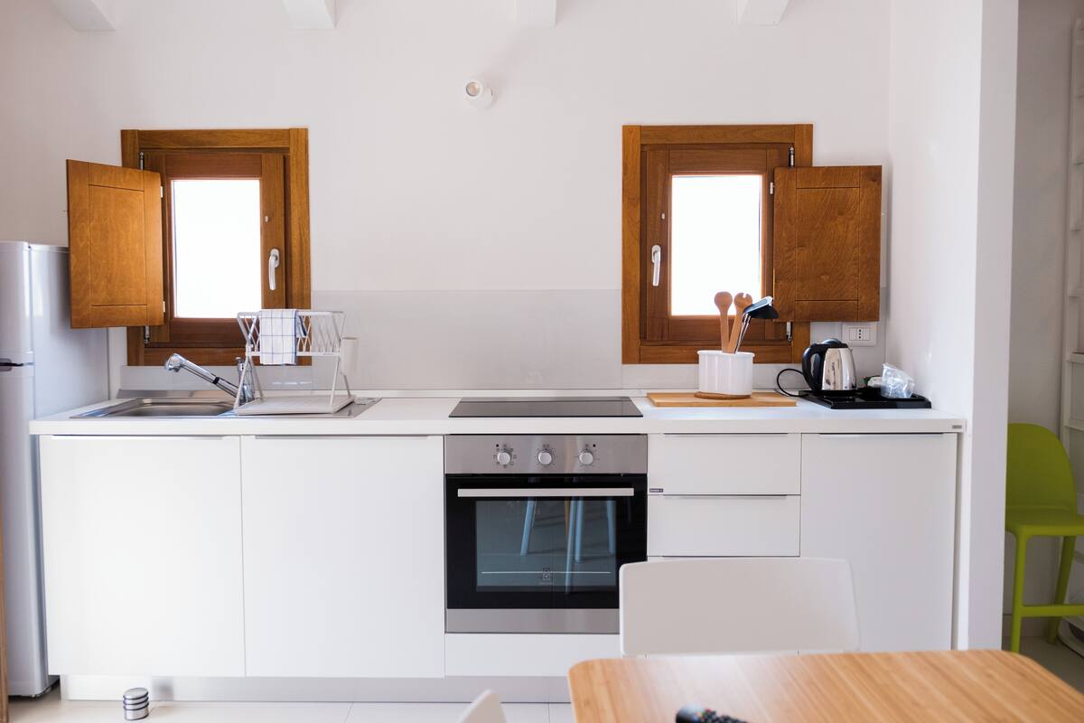 A modern kitchen with white cabinetry, a built-in oven, a sink, and a window above the counter.