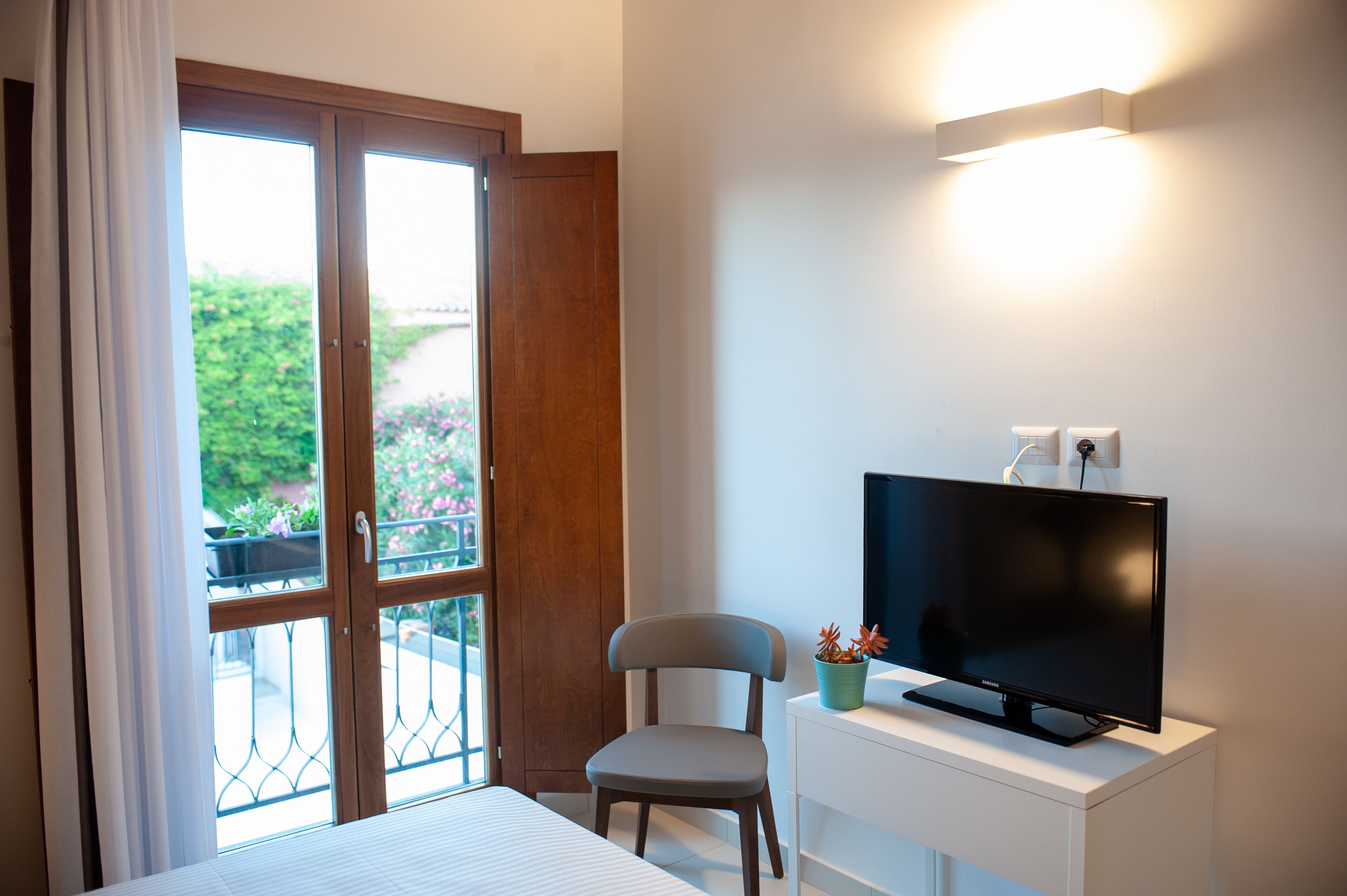 Una habitación con cama, un escritorio con televisor, una silla y una ventana con cortinas.