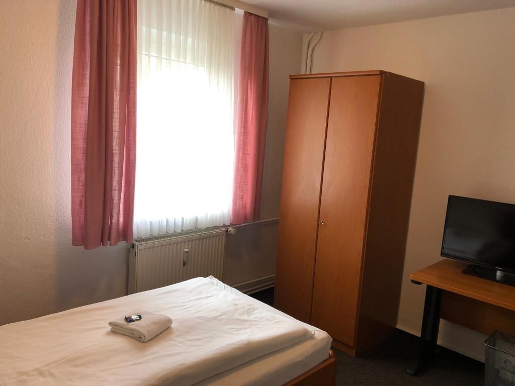 A hotel room with a bed, a wardrobe, a desk with a television, and a window with curtains.