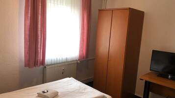 A hotel room with a bed, a wardrobe, a desk with a television, and a window with curtains.