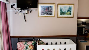 Une pièce avec un berceau blanc, un téléviseur fixé au mur et deux tableaux encadrés.