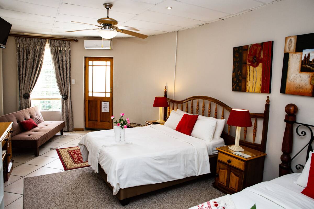 A hotel room with a bed, a chair, a desk, a lamp, and artwork on the wall.