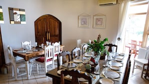 Une salle à manger avec une longue table en bois dressée pour le repas, entourée de chaises blanches.