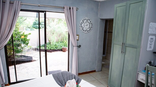 Une chambre d’hôtel avec un lit, une armoire, une horloge au mur et une vue sur le jardin extérieur.