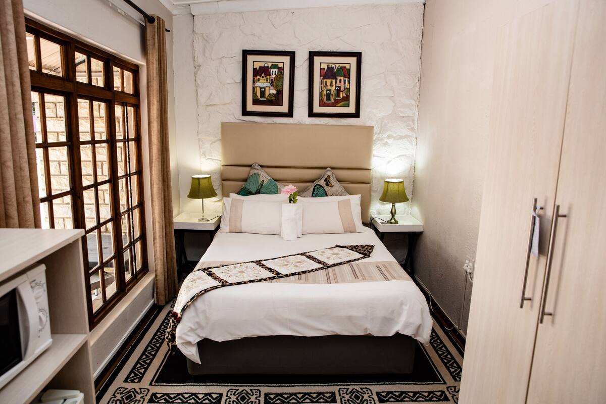A bedroom with a bed, two nightstands, a window with curtains, and two framed pictures on the wall.