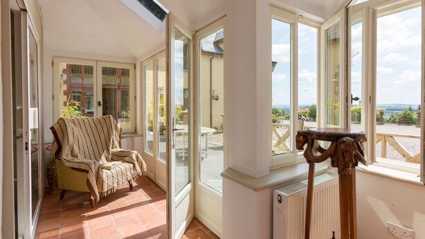 A sunlit room with a chair, a table, and a view through large windows. - Charming Old Farmhouse, Beautifully Restored - ideal base to explore SW Ireland (Coachford)