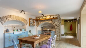 A kitchen with a stone archway, blue cabinets, and a wooden table with chairs. - Charming Old Farmhouse, Beautifully Restored - ideal base to explore SW Ireland (Coachford)