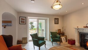 A spacious living room with a fireplace, two green armchairs, a wooden coffee table, and a red suitcase. - Charming Old Farmhouse, Beautifully Restored - ideal base to explore SW Ireland (Coachford)