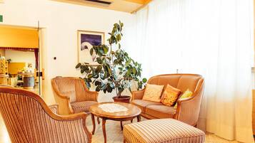 A cozy living room with striped wicker furniture, a round coffee table, and a large potted plant.